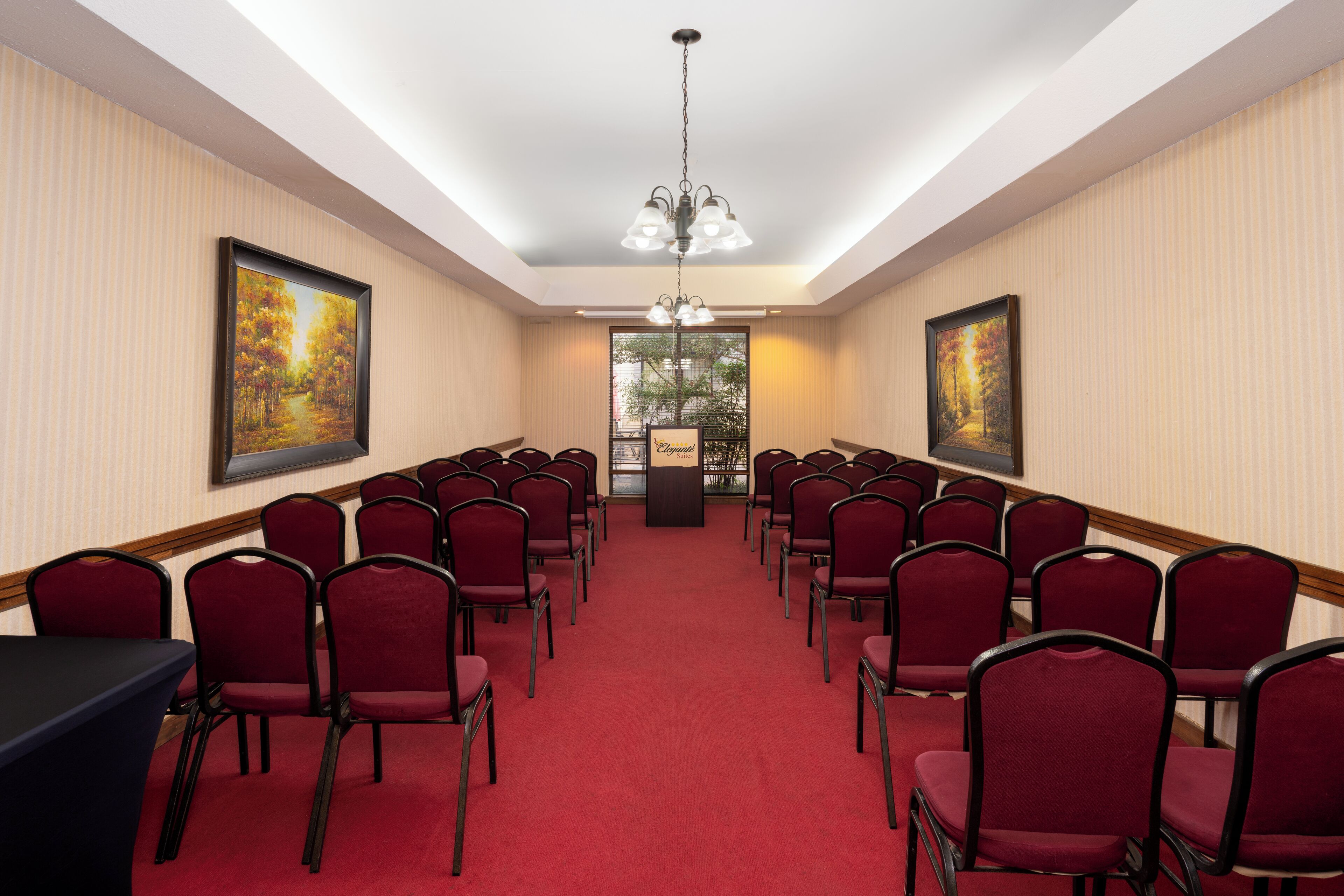 A conference room with rows of red chairs, a podium, and two large paintings on the walls.