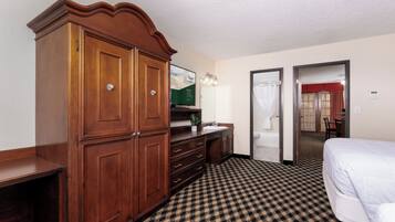 A hotel room with a large wooden wardrobe, a checkered floor, a bed, a desk, and a bathroom visible through an open door.