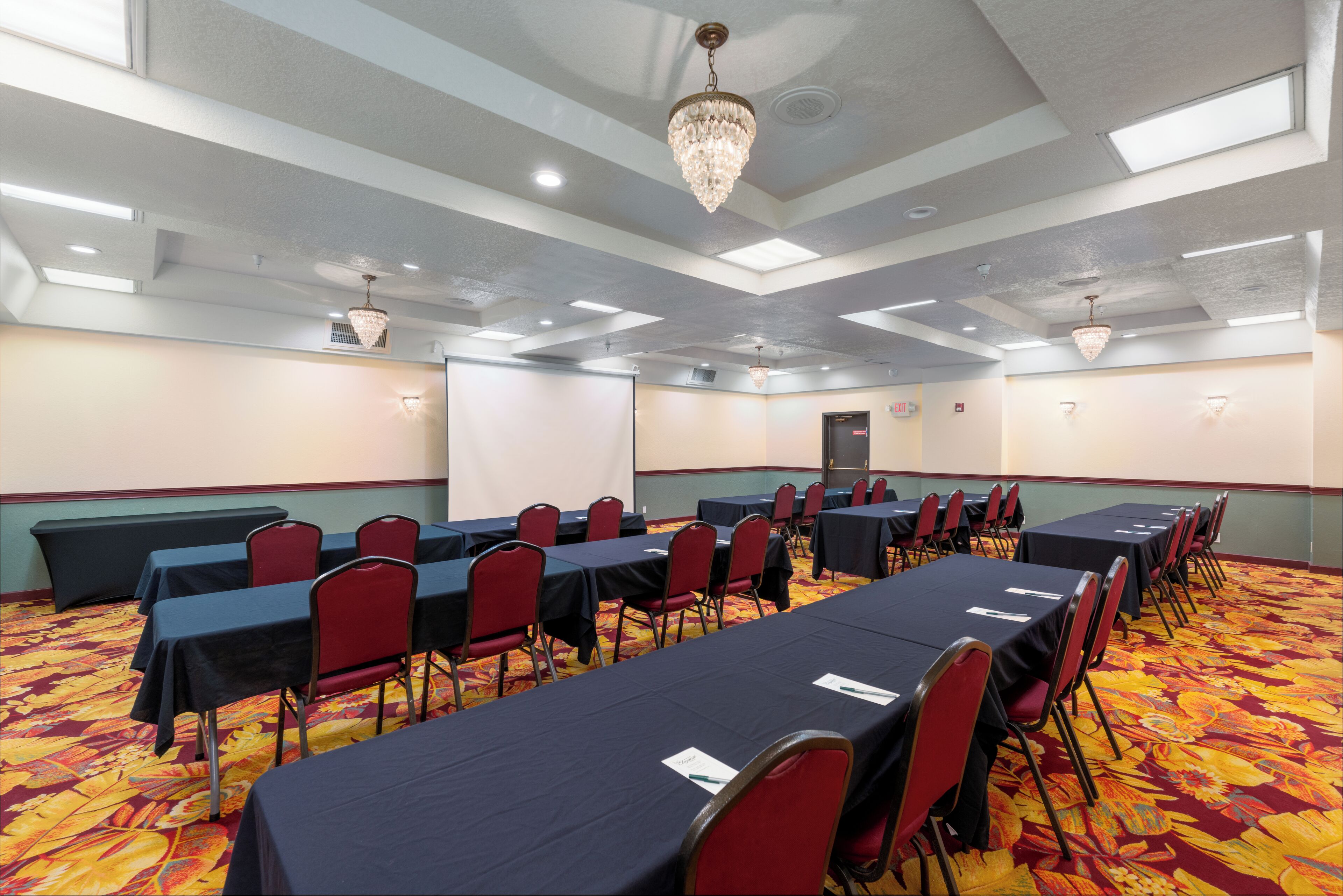 Une salle de conférence équipée de tables et de chaises, dotée d’un sol recouvert de moquette et d’un lustre.