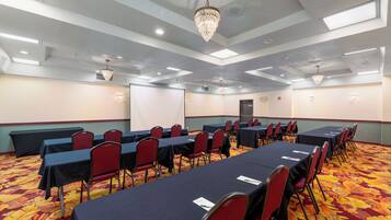 Un salón de conferencias con mesas y sillas, piso alfombrado y un candelabro.
