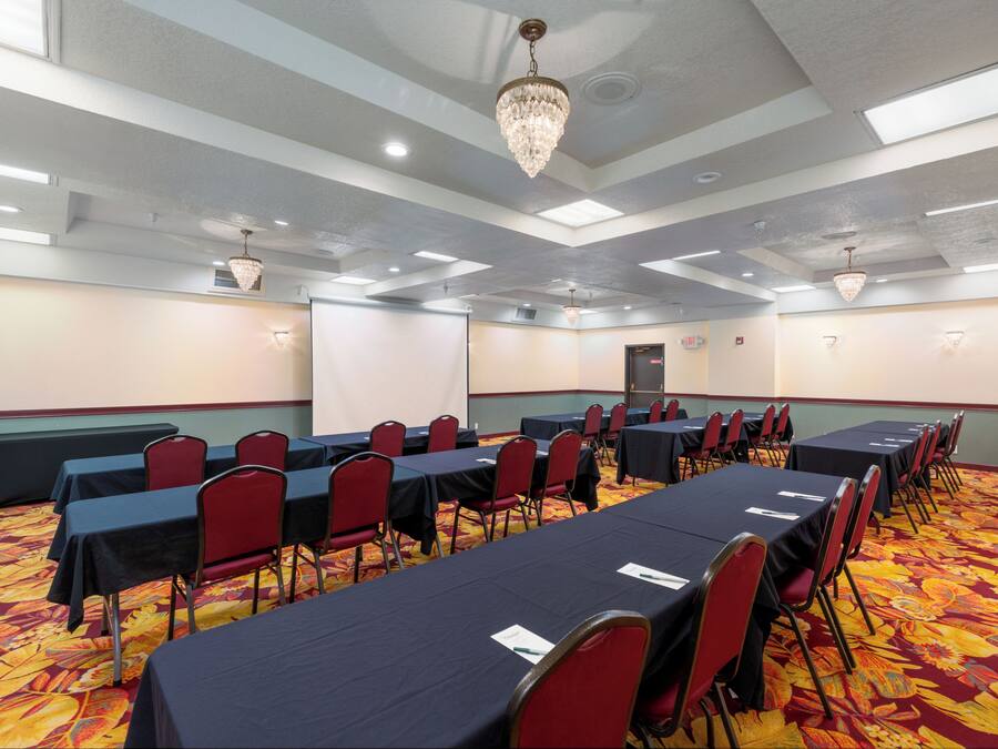 Un salón de conferencias con mesas y sillas, piso alfombrado y un candelabro.