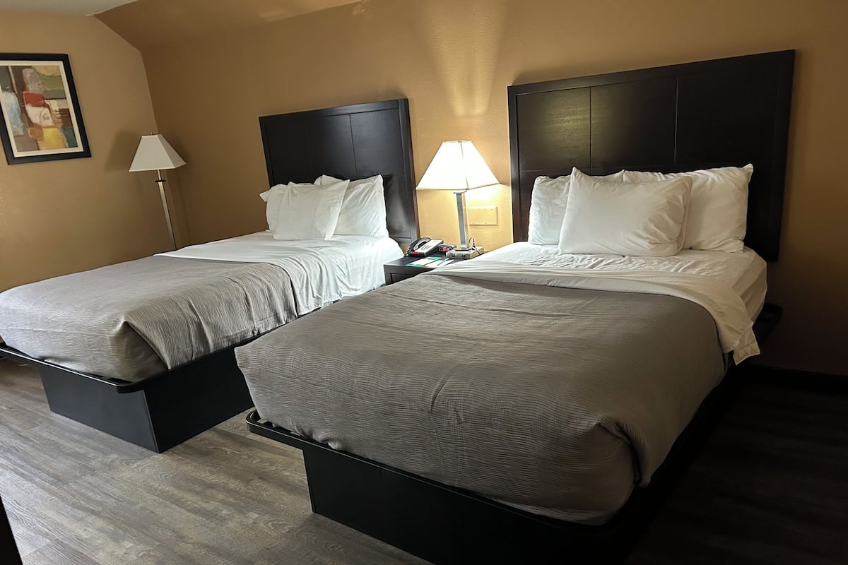 A hotel room with two single beds, each with a wooden headboard, a bedside table, and a lamp.