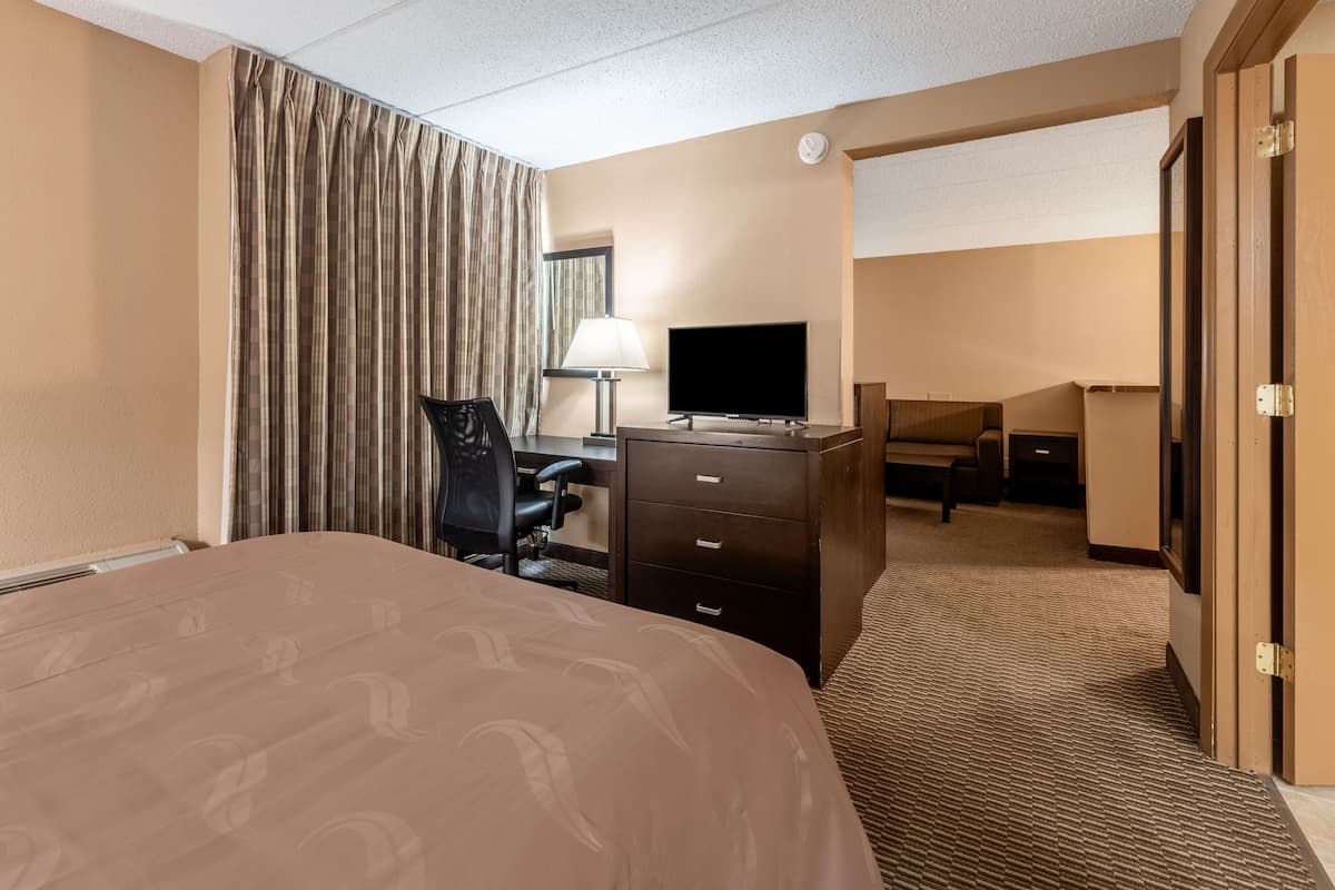 A hotel room with a large bed, a desk with a TV, a chair, and a lamp.