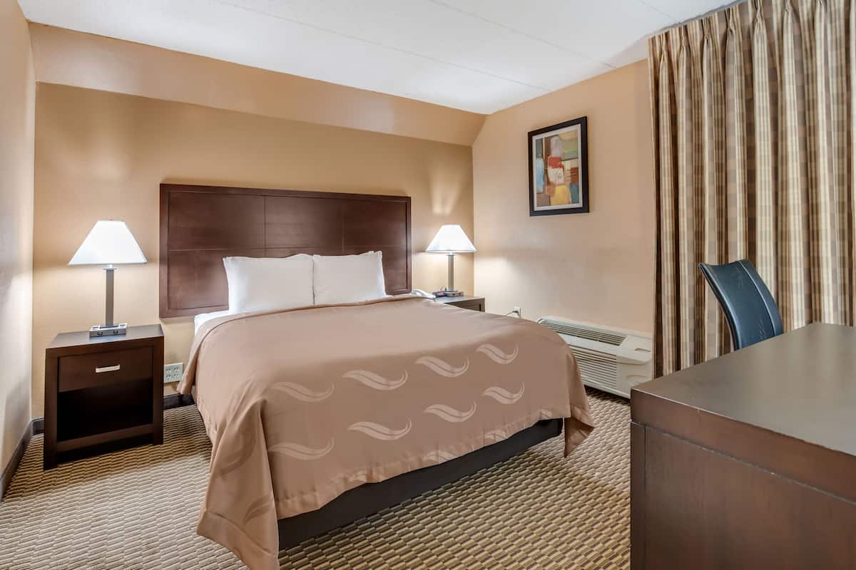 A hotel room with a bed, two bedside tables with lamps, a desk, and a chair.