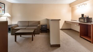Una habitación de hotel compacta con sofá, una mesita, una kitchenette con microondas y una lámpara.