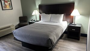 Una cama bien hecha con cabecera, dos mesitas de noche con lámparas, una silla y un aire acondicionado de pared.