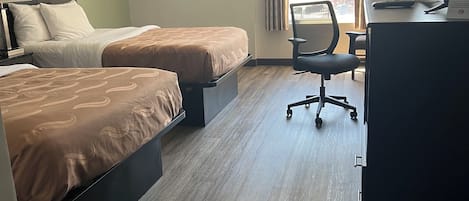 Et hotelværelse med to senge, et skrivebord, en stol og et vindue med gardiner.