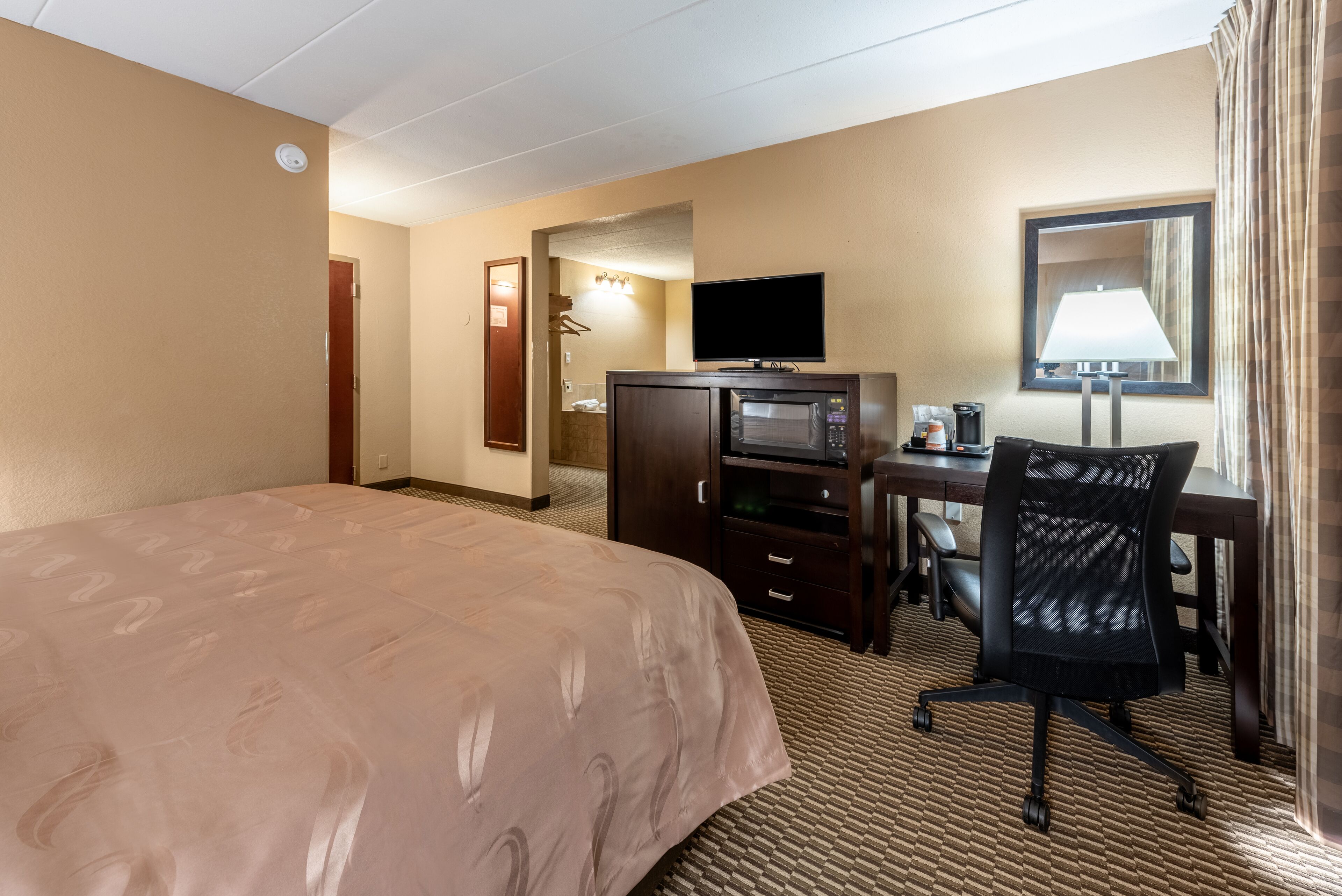 A hotel room with a large bed, a desk with a computer, a television, and a microwave.