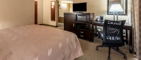 A hotel room with a large bed, a desk with a computer, a television, and a microwave.