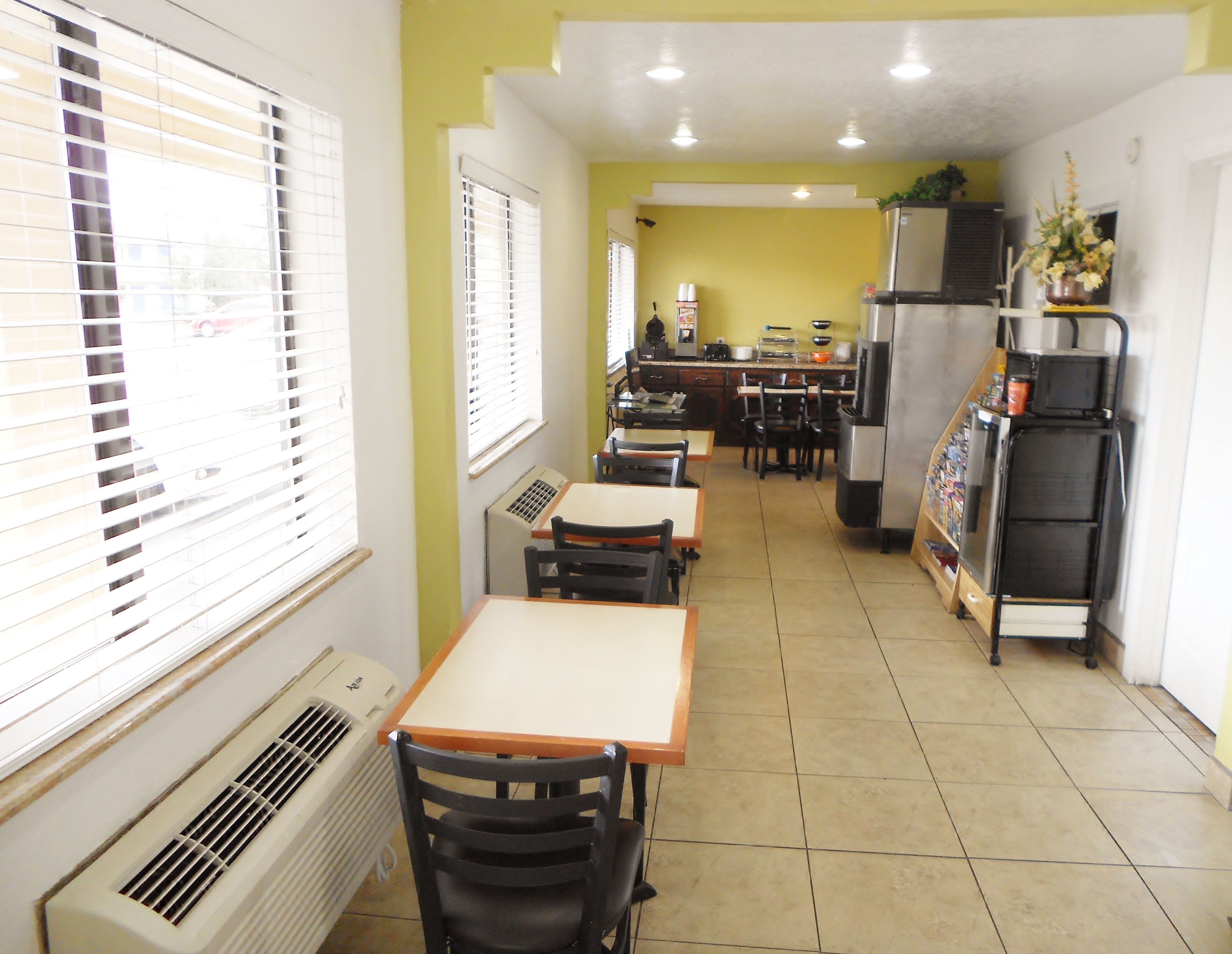 A bright dining area with tables and chairs, a kitchen in the background, and a vending machine.