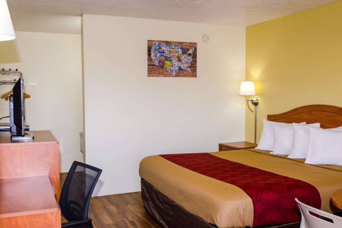 A hotel room with a bed, a desk, a chair, a lamp, and a wall art piece.