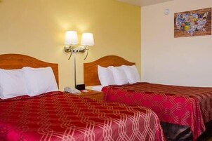 Habitación de hotel con dos camas, cada una con una colcha roja estampada, una mesita de noche con lámpara y un reloj de pared.