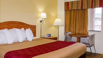 Una habitació d'hotel amb llit, abacines, taula petita i cadira.