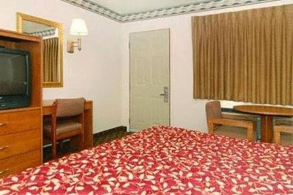 A hotel room with a bed, a desk, a chair, a television, a lamp, and a door.