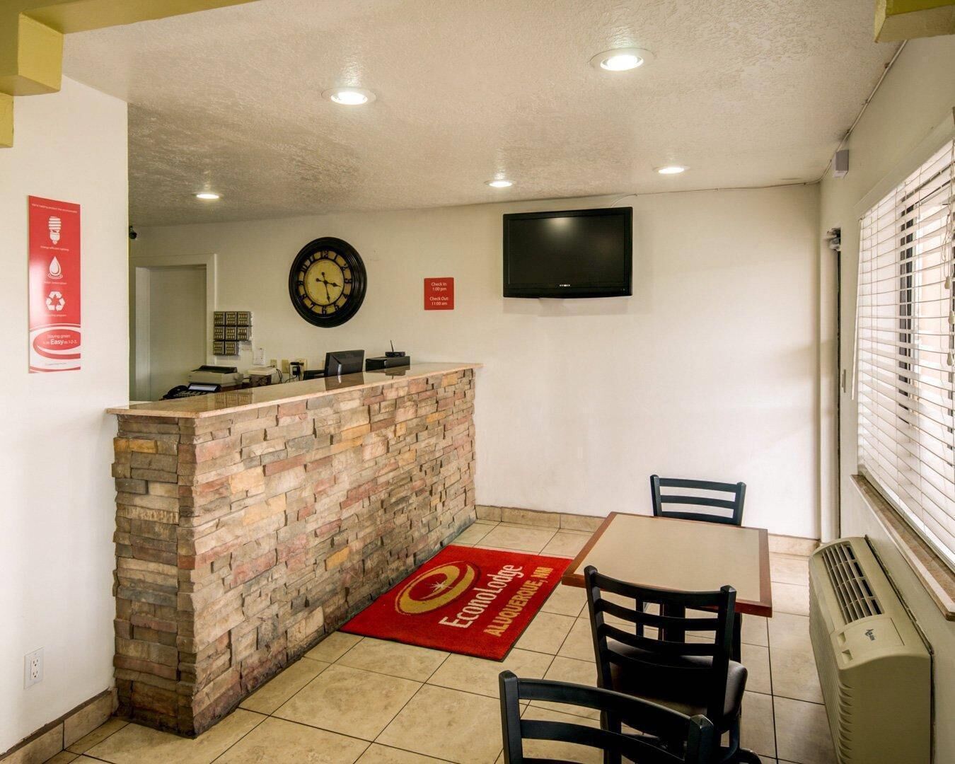 A reception area with a stone counter, a clock, a television, and a red carpet with a logo.