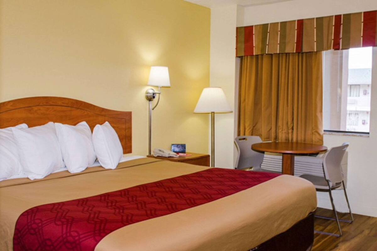 A hotel room with a bed, bedside lamps, a small table, and a chair.