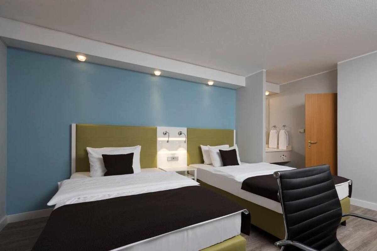 Habitación de hotel con dos camas, un escritorio, una silla y un baño.