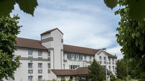 A multi-story hotel with a modern design, featuring a central entrance with glass doors, surrounded by greenery and a paved driveway. - Peine Salzgitter Hotel by Belvilla (Peine)