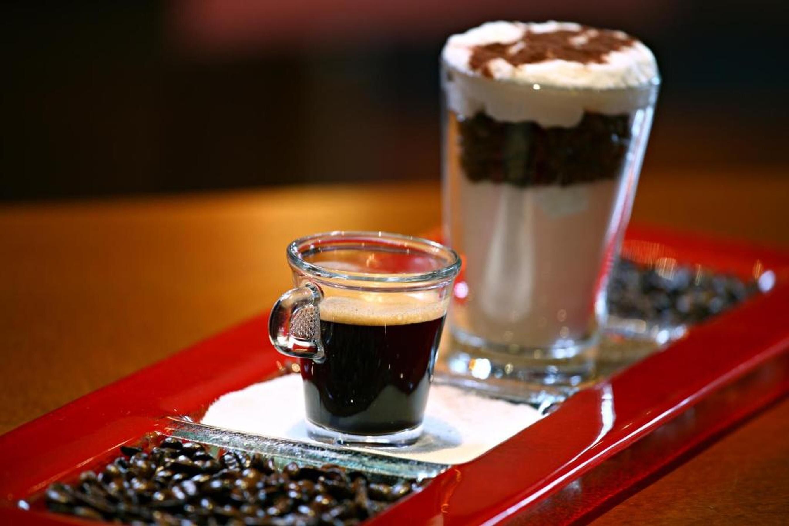 Een glas donkere vloeistof, mogelijk koffie, en een gelaagd drankje met slagroom op een dienblad.