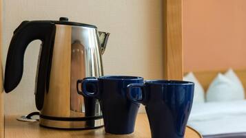 Une bouilloire en acier inoxydable et deux tasses bleu foncé sur une table en bois, dans une chambre d’hôtel.