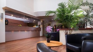 A reception area with a wooden reception desk, a reception sign, a potted plant, and leather chairs. - Peine Salzgitter Hotel by Belvilla (Peine)