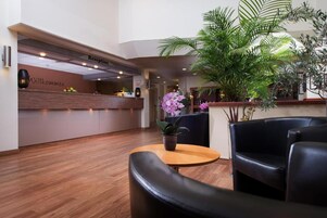 Un área de recepción con un mostrador de madera, un letrero de recepción, una planta en maceta y sillones de cuero.