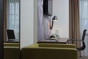 A hotel room with a desk, two chairs, a lamp, a television, and a window with curtains.