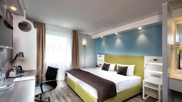 Una habitación de hotel con cama, escritorio, silla y ventana con cortinas.