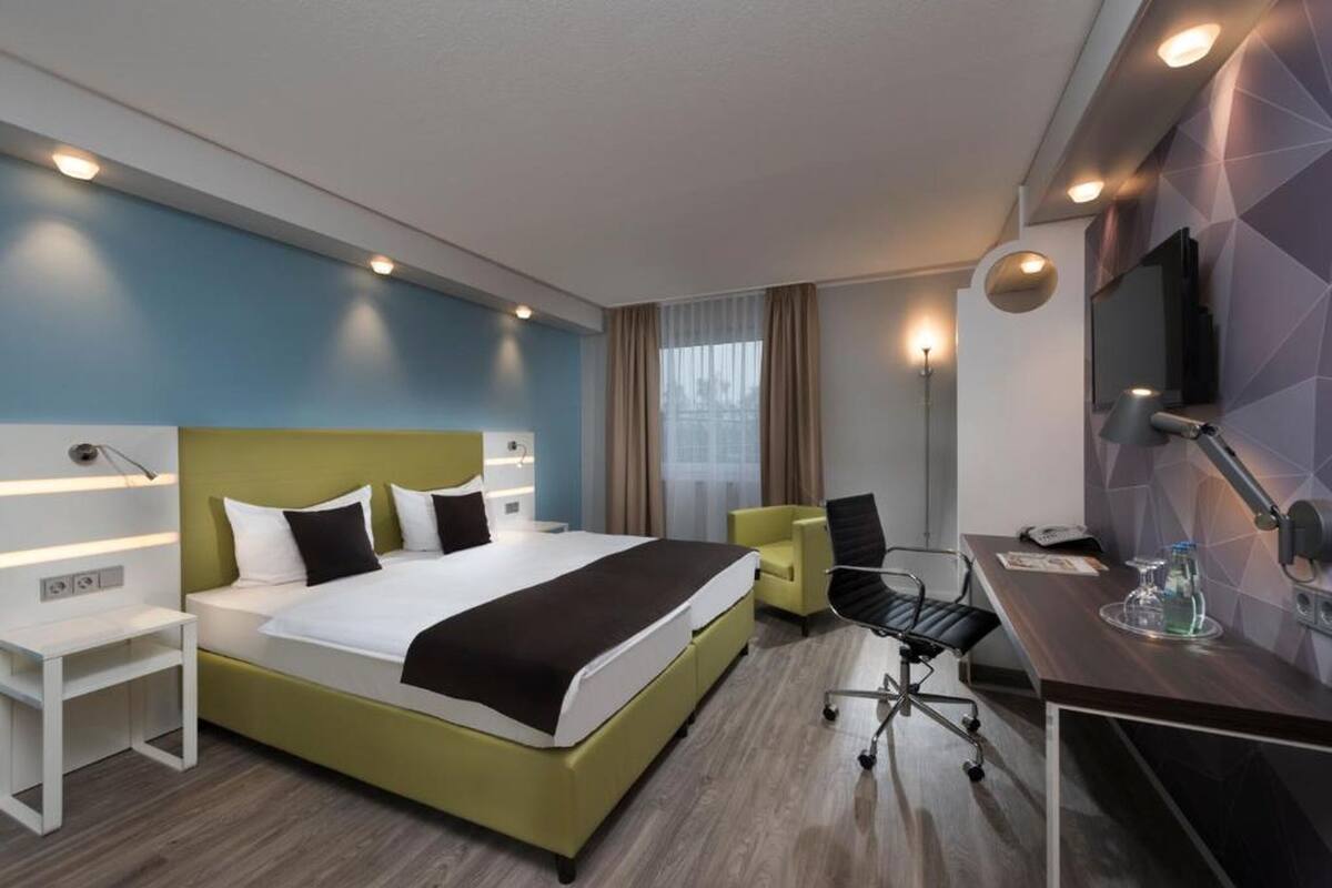 Habitación de hotel con cama, escritorio, silla y televisor.