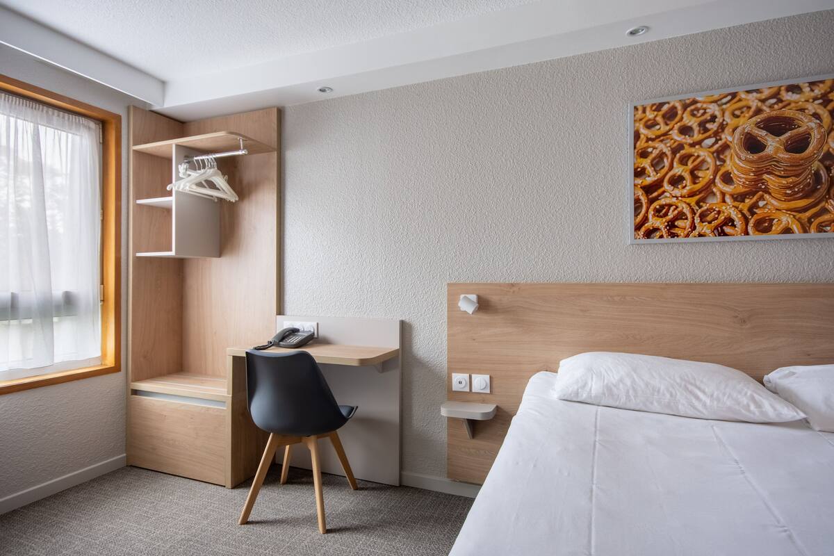 Une chambre d’hôtel comprenant un lit, un bureau avec une chaise, une armoire et un tableau au mur.