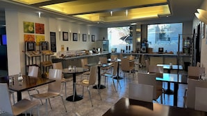 Un café moderne avec de nombreuses tables et chaises, un comptoir où sont exposés des plats, et des tableaux encadrés accrochés aux murs.
