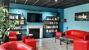 Un espace de détente moderne avec des sièges rouges, une cheminée, une bibliothèque et un téléviseur.