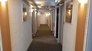 Un couloir d’hôtel avec des revêtements de sol en moquette, des portes des deux côtés et des appliques murales.