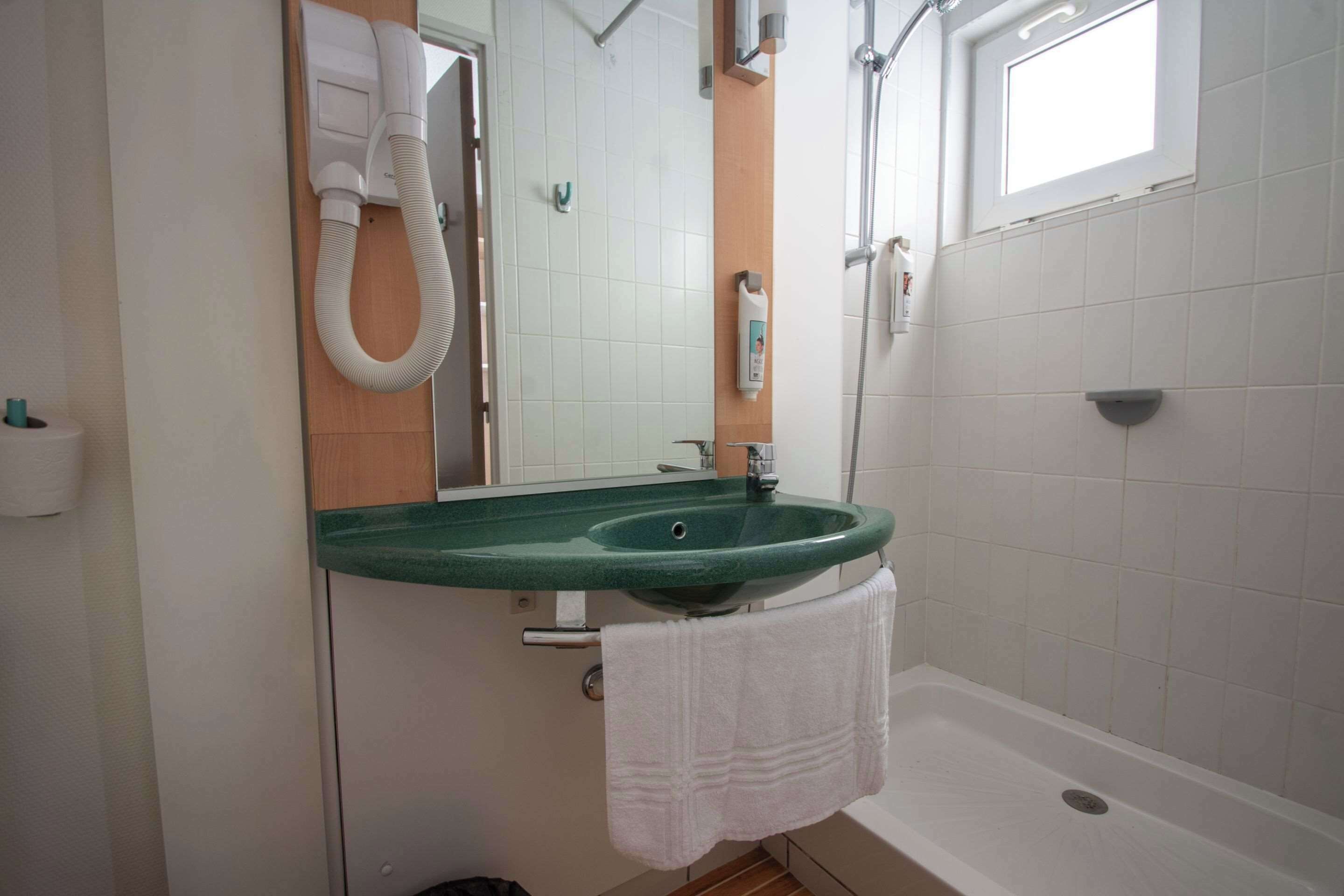 Uma casa de banho com uma sanita, chuveiro, toalheiro, espelho e lavatório verde.