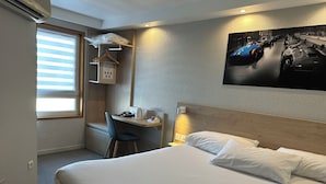 Une chambre d’hôtel équipée d’un lit, d’un bureau, d’une chaise et d’un téléviseur fixé au mur.