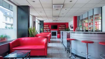Eine moderne Bar mit roten Sitzplätzen, einem Glastisch und einer Bar, die mit Hocker bestückt ist.
