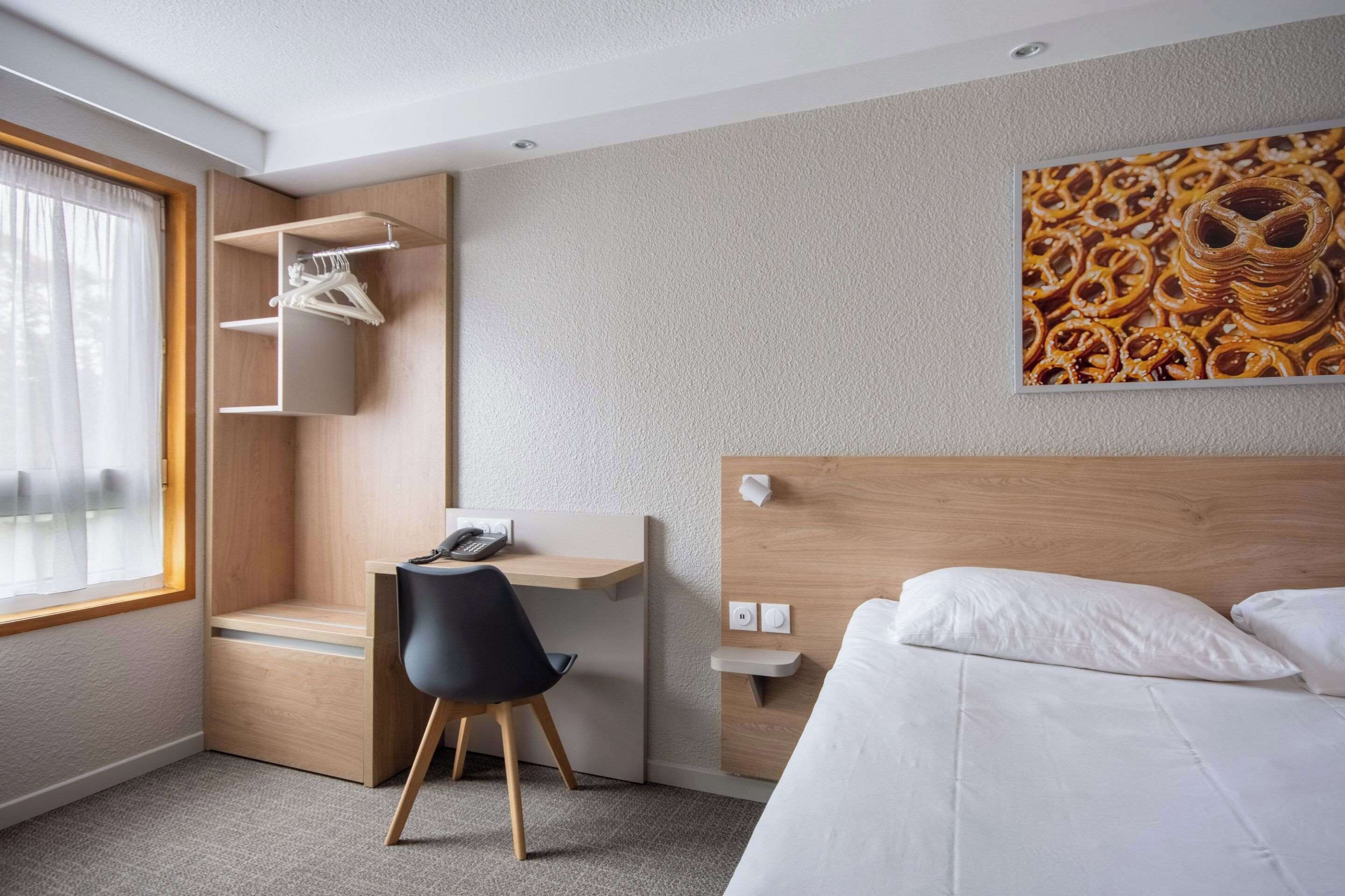 Una moderna camera d'albergo con un letto, una scrivania, una sedia, un armadio e un quadro appeso al muro.