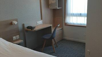 A hotel room with a bed, a desk, a chair, a wardrobe, and a window with curtains.