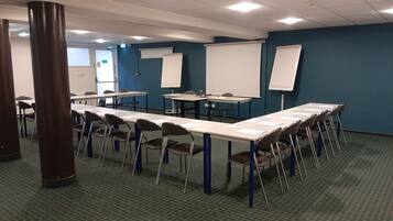 Ein Konferenzraum mit langem Tisch, Stühlen, einer Whiteboard und einer Projektionsleinwand.