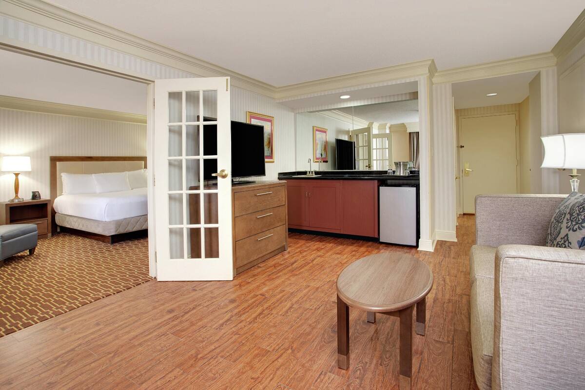 A hotel room with a bed, a small table, a sofa, a kitchenette, and a bathroom.