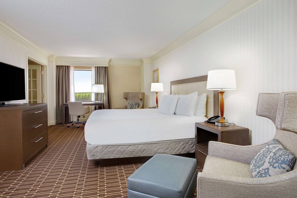 A hotel room with a bed, a desk, a chair, a TV, and a lamp.