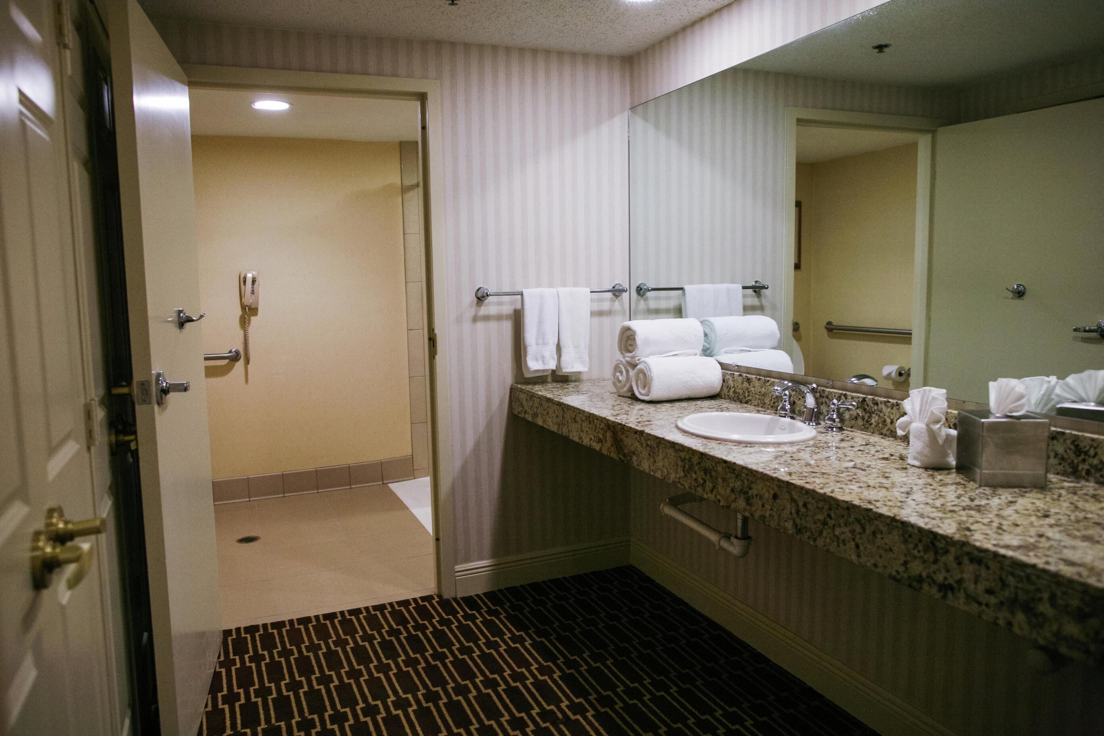 A hotel bathroom with a sink, mirror, towels, and a patterned floor.