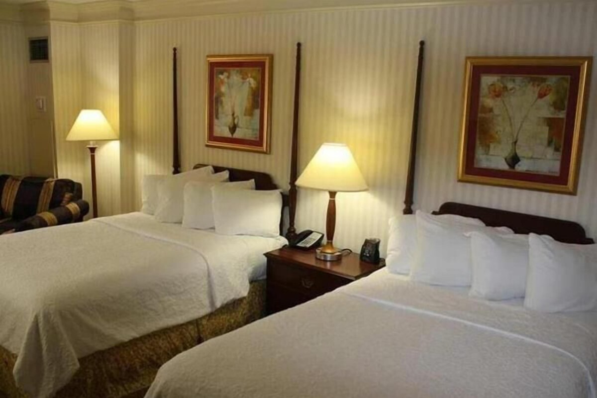 A hotel room with two beds, a nightstand with a lamp, a telephone, and framed artwork on the walls.