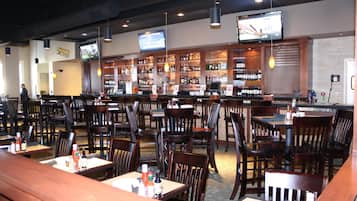 Un restaurant doté de nombreuses tables et chaises, un bar avec des étagères remplies de bouteilles, et un téléviseur fixé au mur.