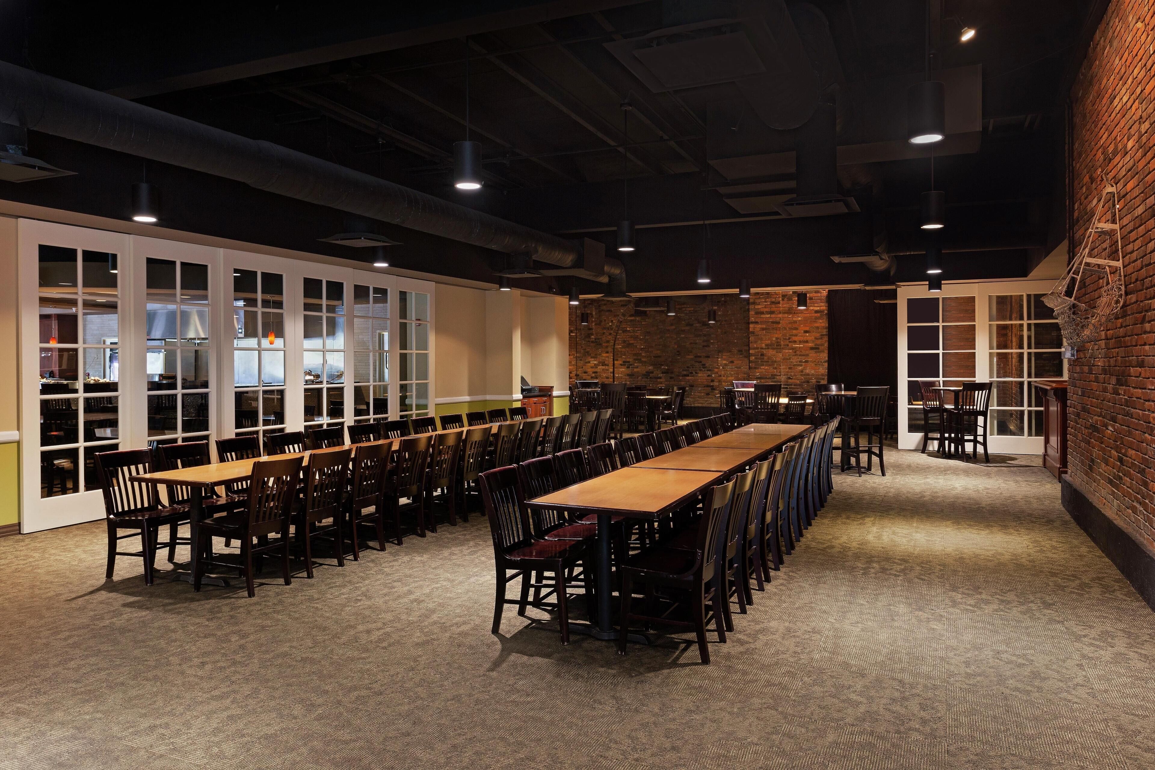 A conference room with long tables and chairs, large windows, and a brick wall.
