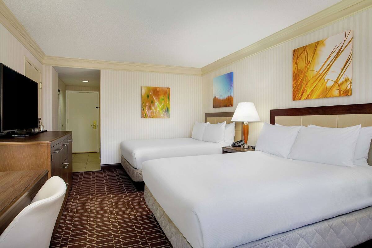 A hotel room with two beds, a desk, a TV, and artwork on the walls.