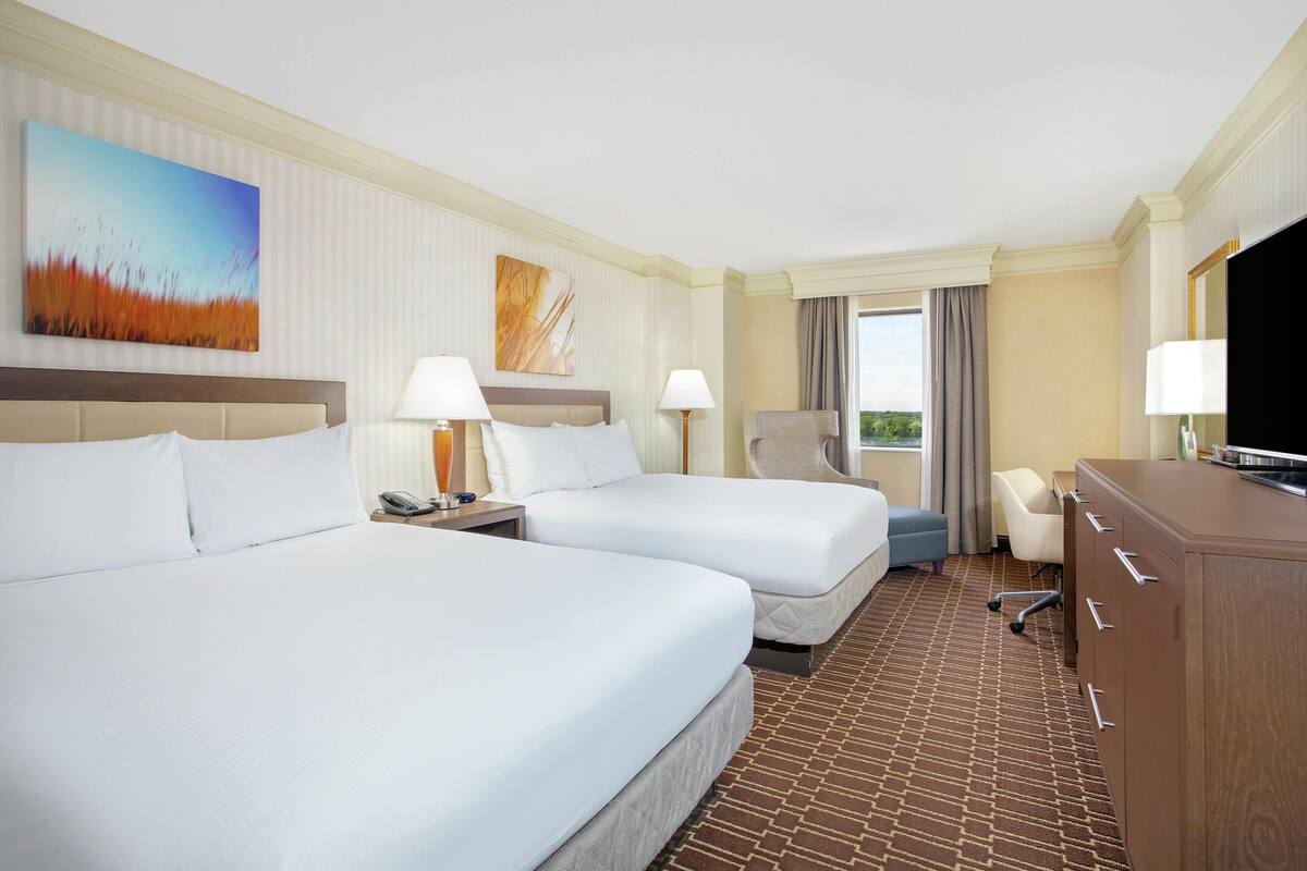 A hotel room with two beds, a desk, a chair, a TV, and a window with curtains.