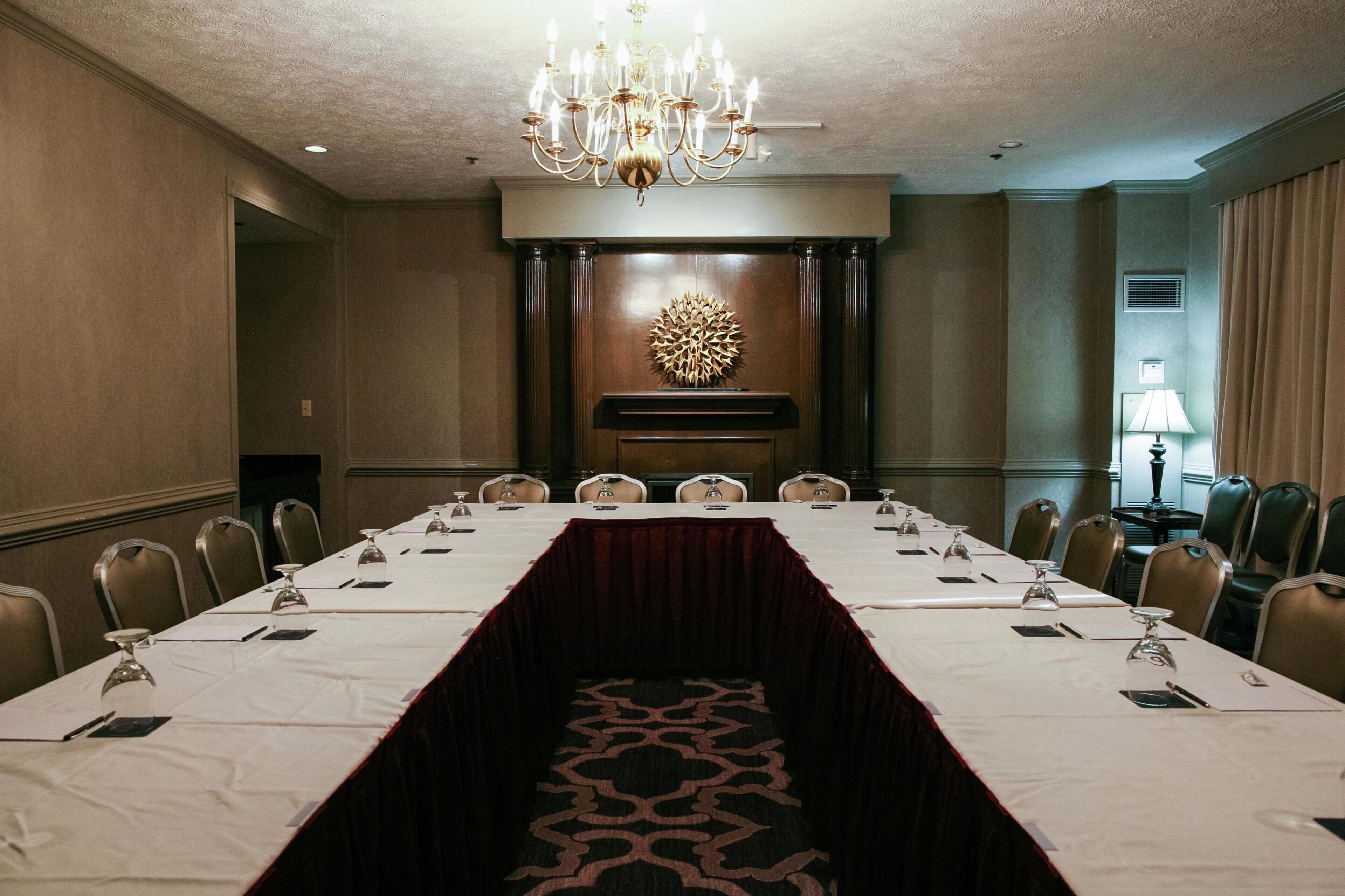 A conference room with a long table, chairs, a chandelier, and a decorative wall piece.