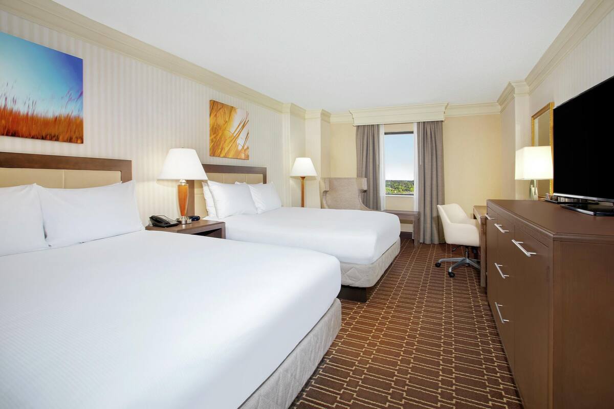 A hotel room with two beds, a desk, a chair, a TV, and a window with curtains.