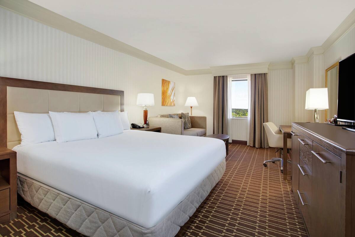 A hotel room with a large bed, a desk, a chair, a television, and a window with curtains.